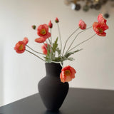 sort keramikvase med orange blomster og vægkunst